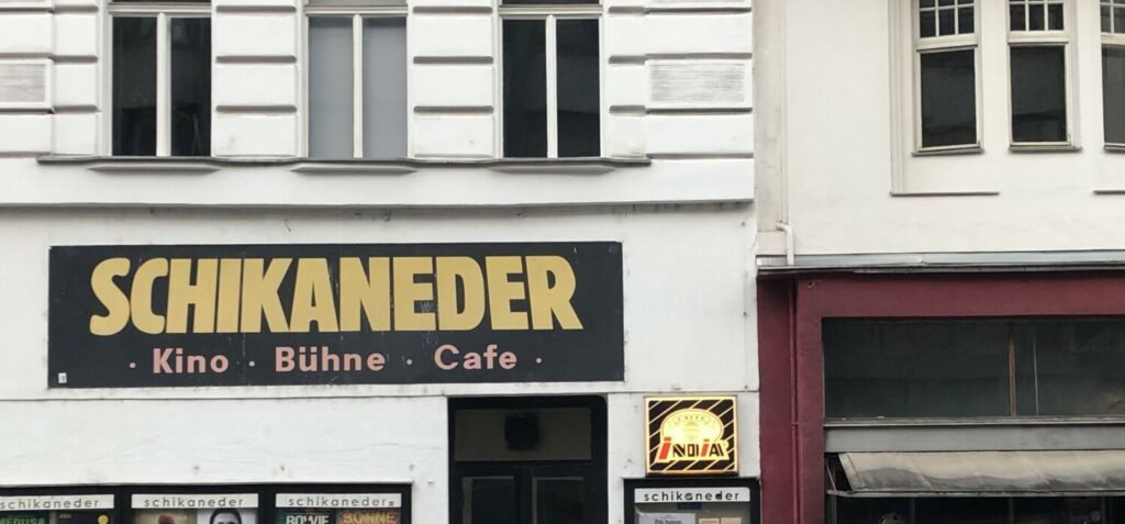 Das Bild einer Hausfassade. In dicker gelber Schrift steht auf einem Schild: "Schikaneder Kino Bühne Cafe".