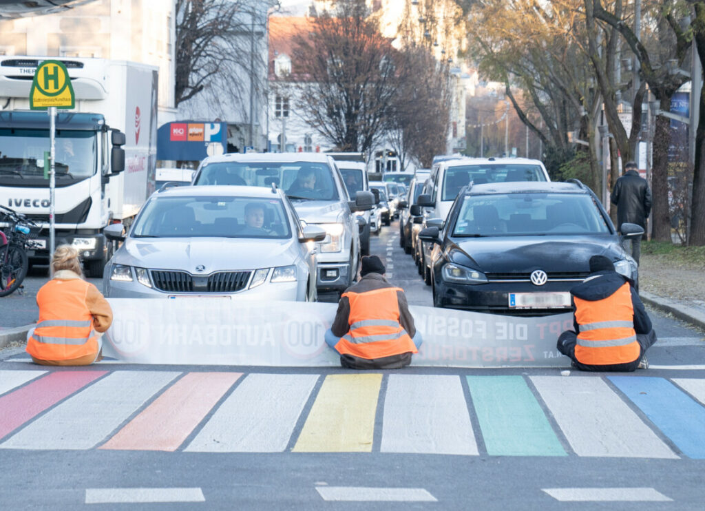 Drei Menschen sitzen auf der Straße und halten den Verkehr auf