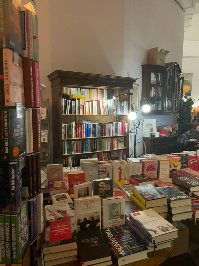 Ein Bild auf dem ein Regal und ein Tisch voll mit Büchern zu sehen ist.